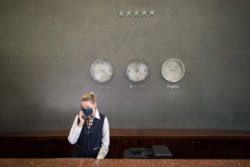 Latin American woman working at a hotelâs reception wearing a facemask and talking on the phone - tourism industry