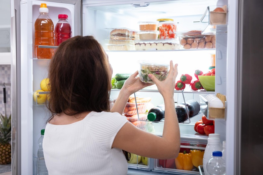 Rear View Of A Young Woman Taking Food From Refrigerator