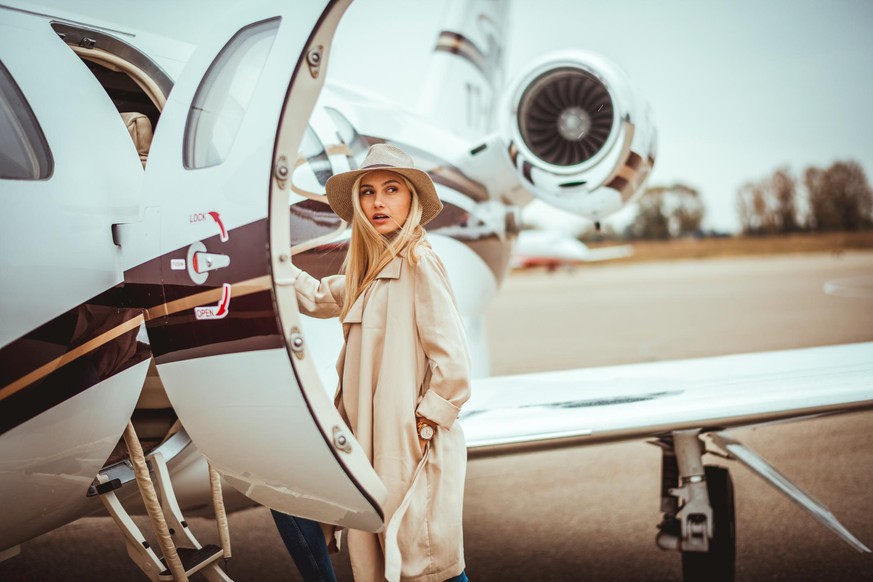 Young rich blonde female entering a private airplane parked on an airport tarmac. She is looking over her shoulder.