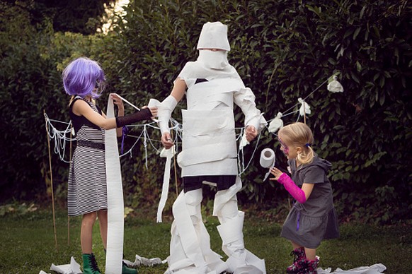 Two children wrapping a third child with toilet paper to play &#039;Mummy Wrap&#039; Halloween game