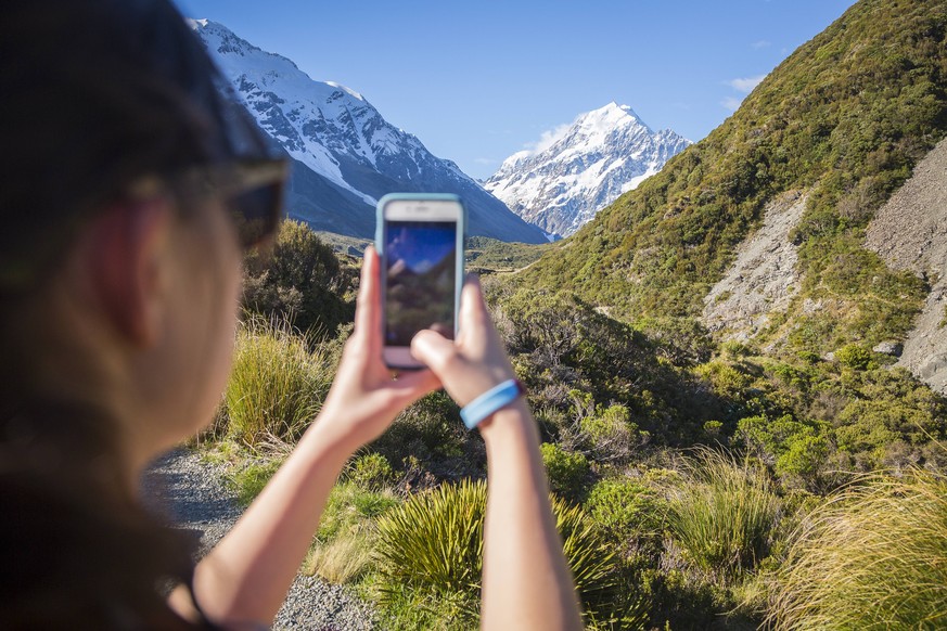 Over the shoulder view of young woman taking picture of Mount Cook with smartphone, Hooker Valley Track, Canterbury, New Zealand, Mt. Cook Village Canterbury New Zealand model released Symbolfoto PUBL ...