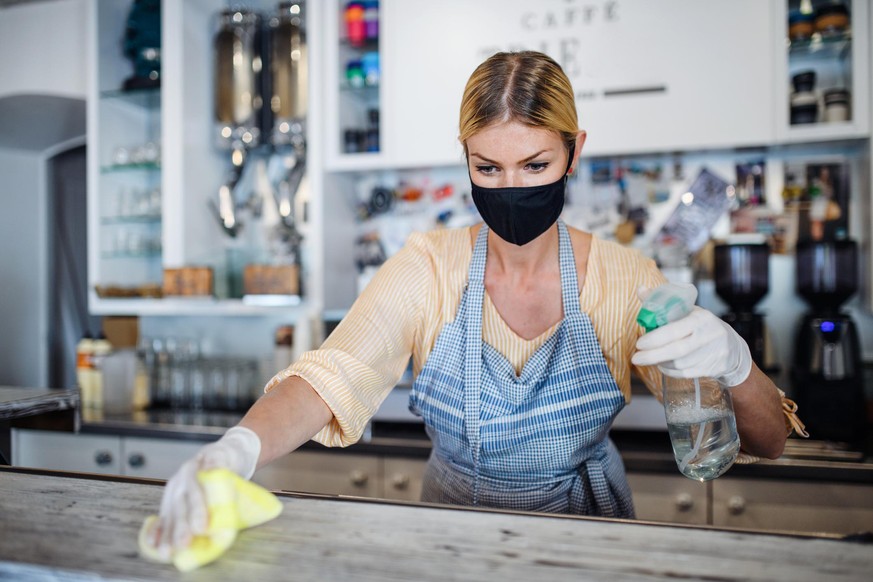 Coffee shop woman owner working with face mask and gloves, cleaning and disinfecting counter.