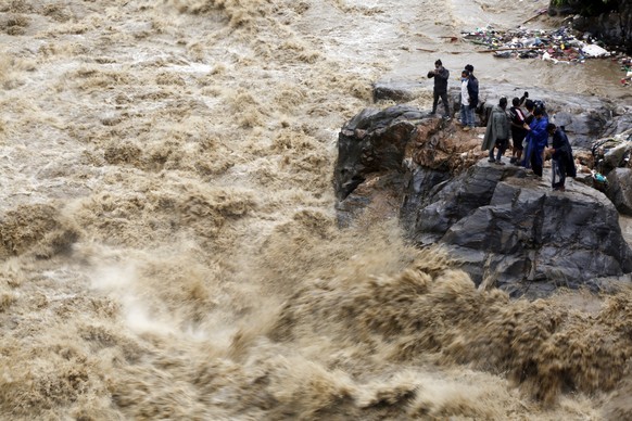 ARCHIV - 21.07.2020, Nepal, Kathmandu: Nepalesen stehen auf einem Felsen am Ufer des �berfluteten Flusses Bagmati und fotografieren die Str�mung. Heftiger Monsunregen hatte in Nepal, Indien und Bangla ...