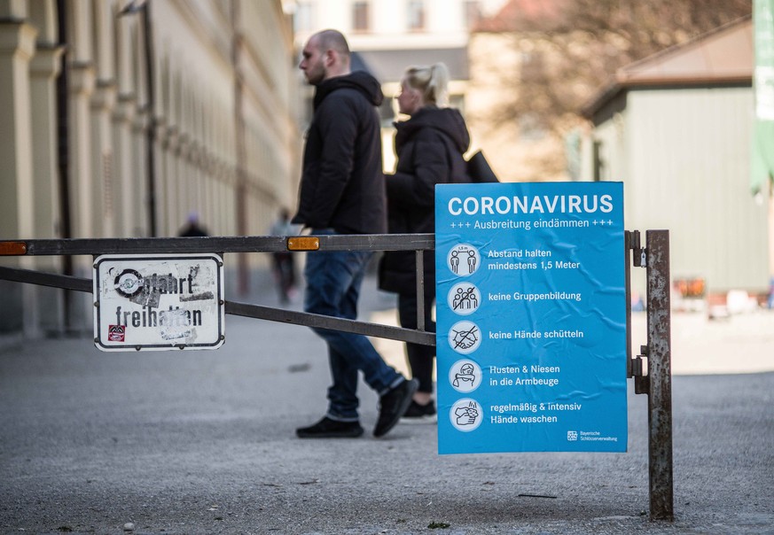 Menschen in München hinter einem Schild, das die Maßnahmen gegen das Coronavirus auflistet.