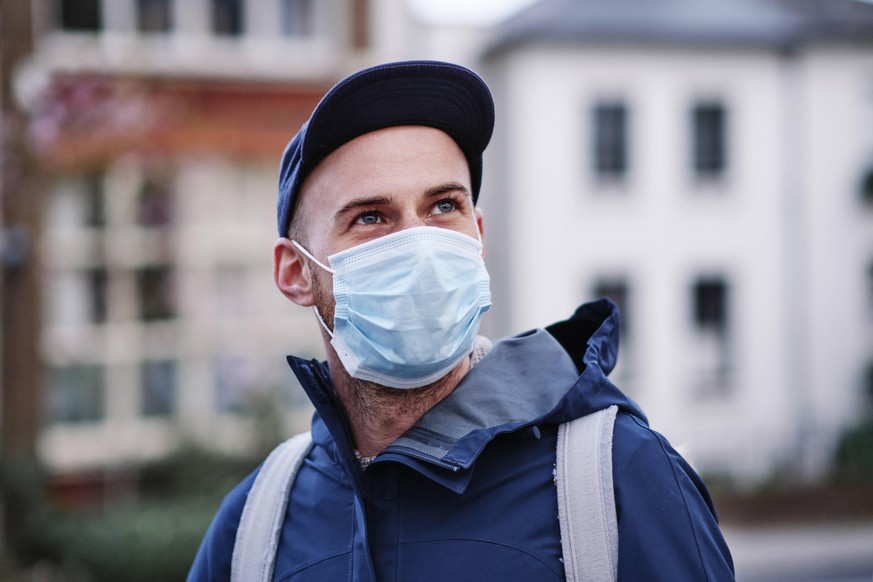 Man with gray eyes looking away while wearing protective face mask during pandemic model released Symbolfoto ASGF00252