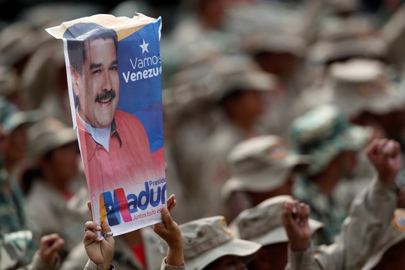 A militia member holds a banner with the image of Venezuela&#039;s President Nicolas Maduro, during a ceremony to mark the 17th anniversary of the return to power of Venezuela&#039;s late President Hu ...
