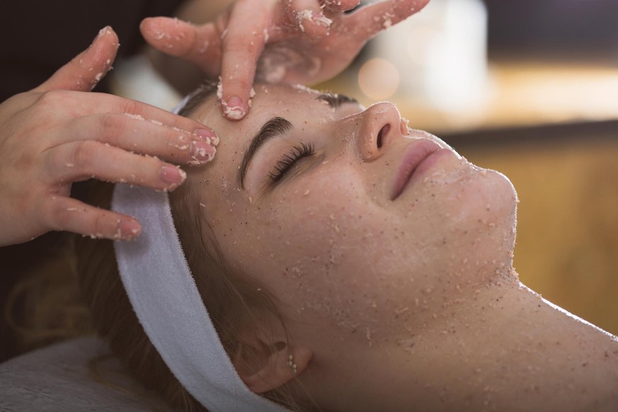 Beautician applying exfoliating salt scrub on woman&#039;s face