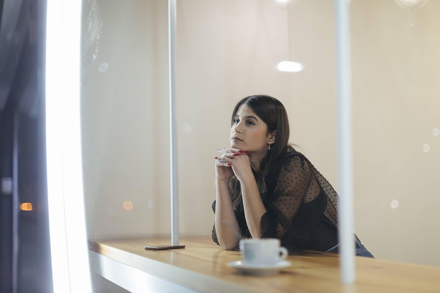 Thoughtful young woman sitting at illuminated coffee shop model released Symbolfoto property released OCAF00473