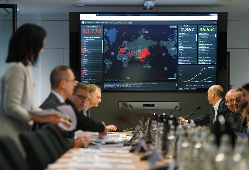 BERLIN, GERMANY - FEBRUARY 28: Members of Germany&#039;s coronavirus emergency task force sit down for a work session while a monitor shows the global spread and human toll of the virus at offices of  ...