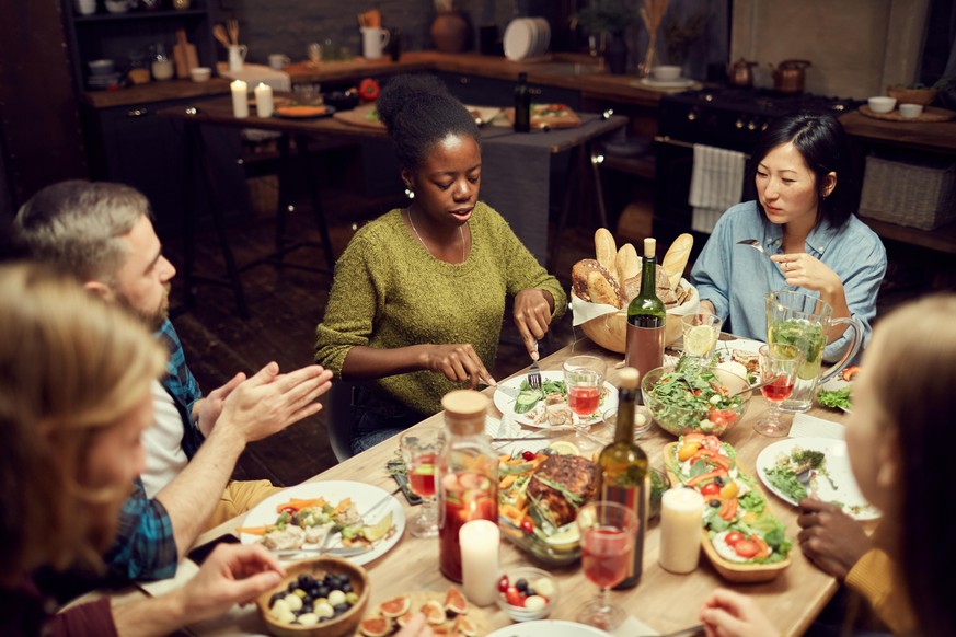 High angle view at multi-ethnic group of people sitting at dinner table together and enjoying delicious food, copy space