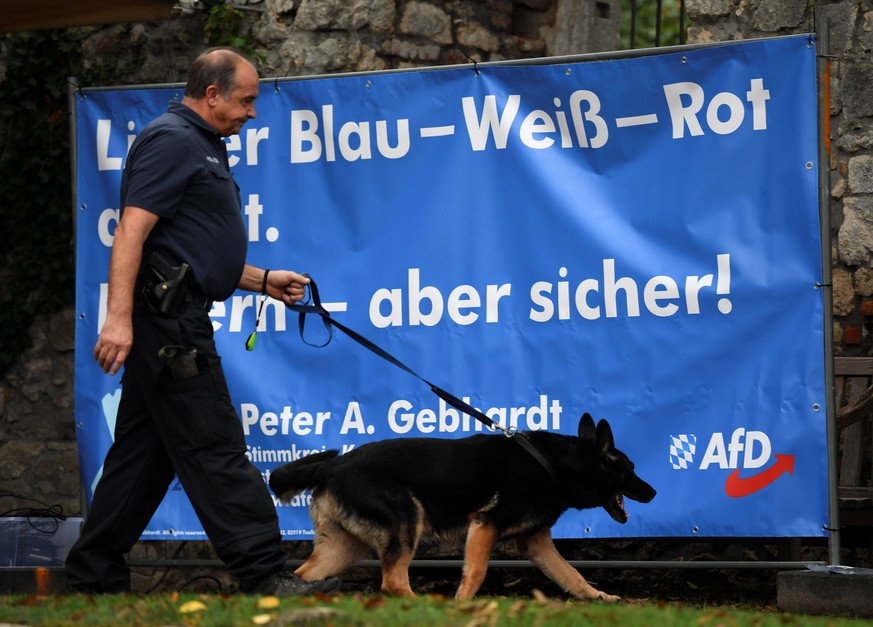 A police officer walks with a dog past a banner of Germany&#039;s anti-immigration party Alternative for Germany (AfD), ahead of the traditional Gillamoos festival in Abensberg, Germany, September 3,  ...