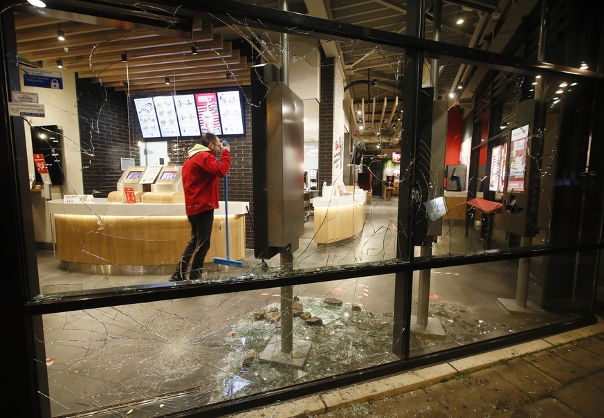 A man cleans up broken glass from the smashed windows in a fast-food restaurant that was damaged in protests against a nation-wide curfew in Rotterdam, Netherlands, Monday, Jan. 25, 2021. The Netherla ...