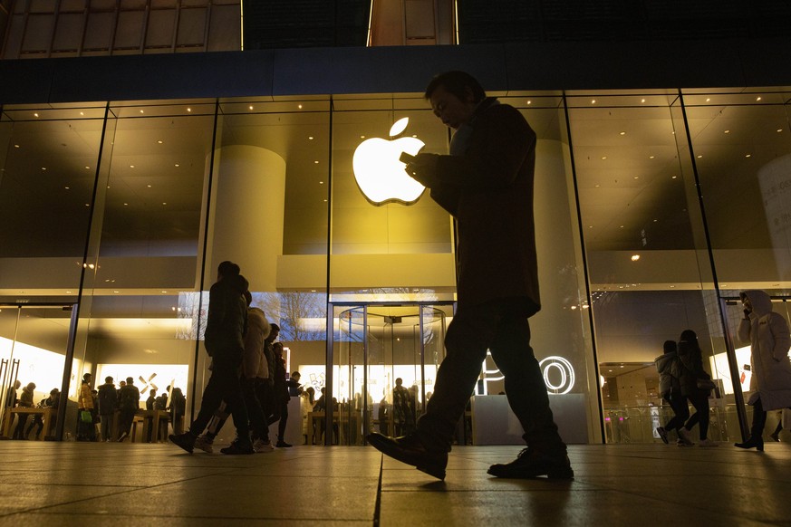 FILE - In this Dec. 13, 2019, file photo, a man looks at his phone as he walks past a store of U.S. tech giant Apple in a retail district in Beijing. As Americans celebrate or fume over the new presid ...