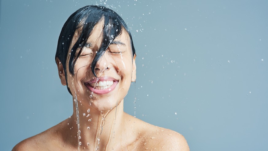 Shot of a young woman having a refreshing shower against a blue background