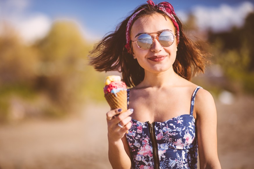 Young brunette woman in boho style eating ice cream at the beach