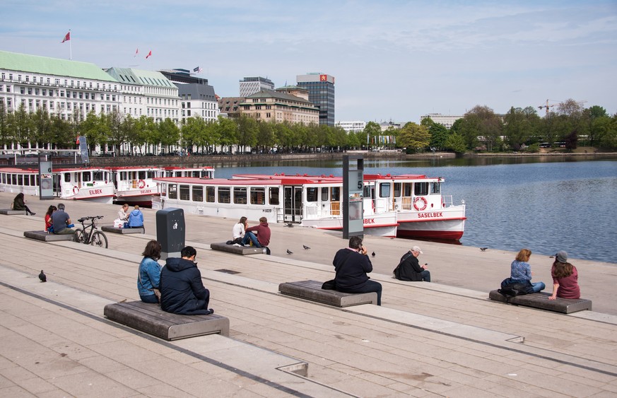 28.04.2020, Hamburg: Menschen sitzen mit Abstand zur Mittagszeit an der Alster am Jungfernstieg in der Sonne. Foto: Daniel Bockwoldt/dpa +++ dpa-Bildfunk +++