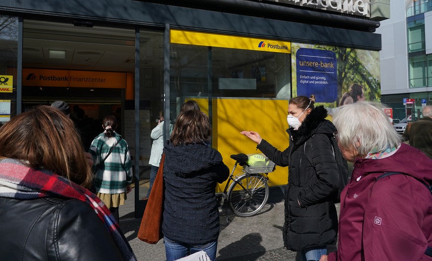 BERLIN, GERMANY - MARCH 18: People, including one woman wearing a protective face mask against the coronavirus, wait to enter a branch of bank Postbank on March 18 in Berlin, Germany. Everyday life in ...