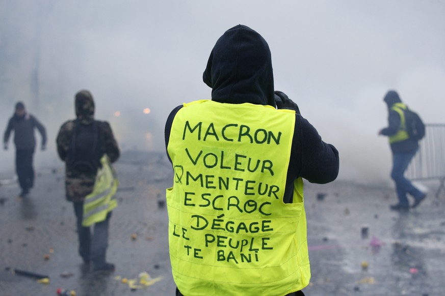 A demonstrator wearing a yellow jacket reading &quot;Macron, thief, lier, crook, go away, the people banishes you&quot; near the Champs-Elysees avenue during a demonstration Saturday, Dec.1, 2018 in P ...