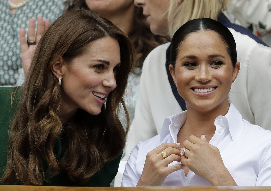 FILE - In this Saturday, July 13, 2019, file photo, Kate, Duchess of Cambridge, left, and Meghan, Duchess of Sussex chat as they sit in the Royal Box on Centre Court to watch the women&#039;s singles  ...