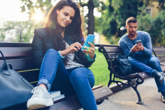 Teenage couple using smartphones in the city park