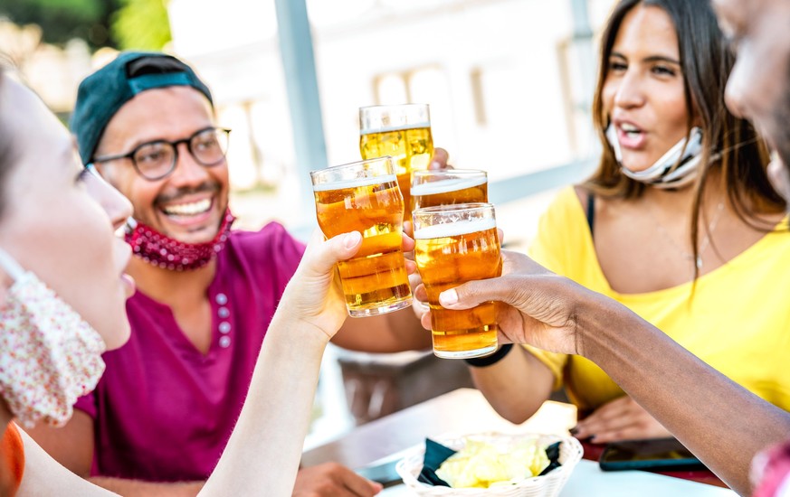 Friends toasting beer glasses with opened face masks - New normal lifestyle concept with people having fun together drinking on happy hour at brewery bar - Bright warm filter with focus on brew pints