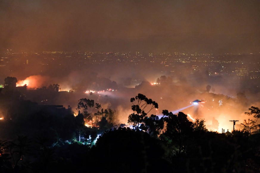October 28, 2019, Los Angeles, California, USA: A helicopter makes a water drop on the Getty Fire in Mandeville Canyon hills in the early hours, the city lights of Los Angeles can be seen behind. The  ...