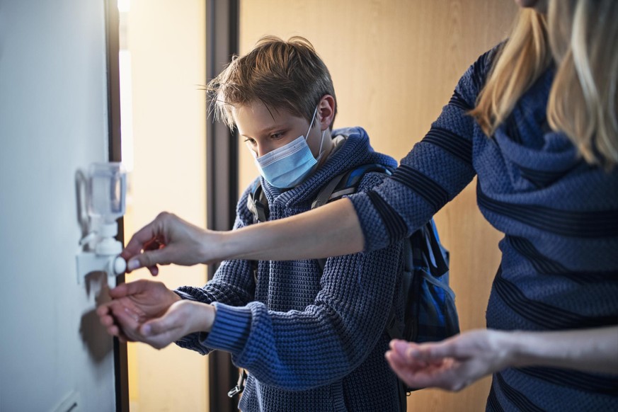 Little boy has returned from school during COVID-19 pandemic and is disinfecting his hands.
The boy is wearing a surgical mask and his mother is helping him.
Nikon D850