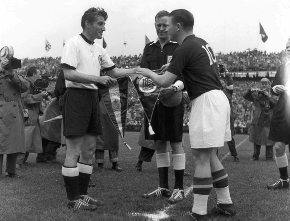 Both captains Fritz Walter, left, and Ferenc Puskas, right, greet one another and the referee William Ling and, according to tradition, swap pennants before the game kicks off, pictured at the final m ...