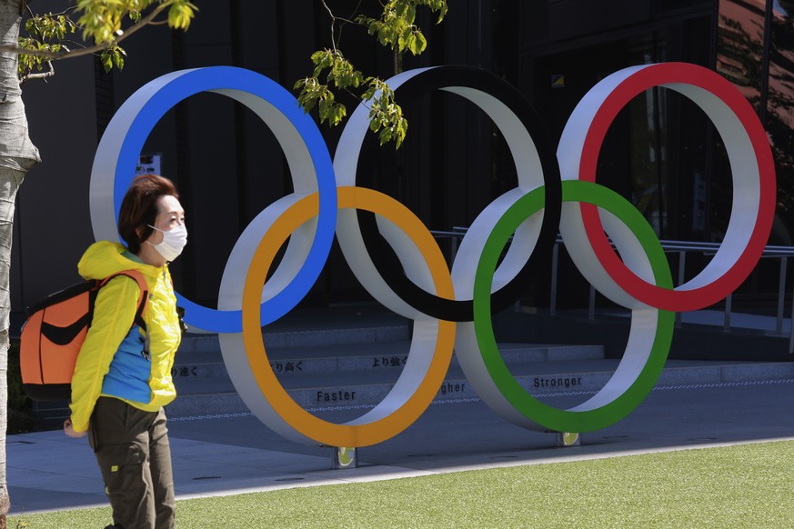 ARCHIV - 10.03.2021, Japan, Tokio: Eine Frau geht mit Maske an den olympischen Ringen vorbei. Fast die H