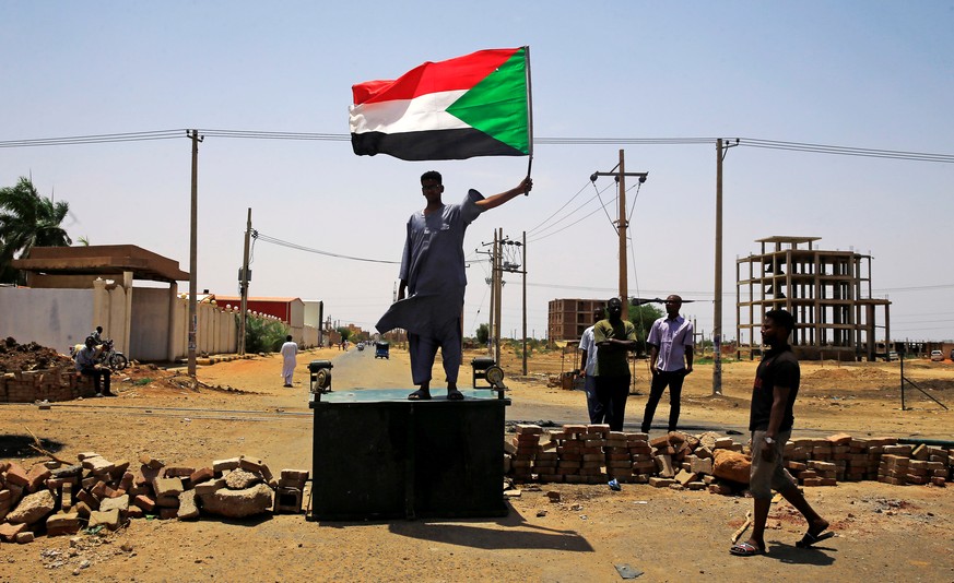 A Sudanese protester holds a national flag as he stands on a barricade along a street, demanding that the country&#039;s Transitional Military Council hand over power to civilians, in Khartoum, Sudan  ...