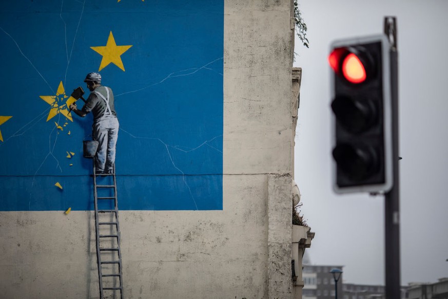 DOVER, ENGLAND - AUGUST 29: A red traffic light in front of a painted mural by British graffiti artist Banksy, depicting a workman chipping away at one of the stars on a European Union (EU) themed fla ...