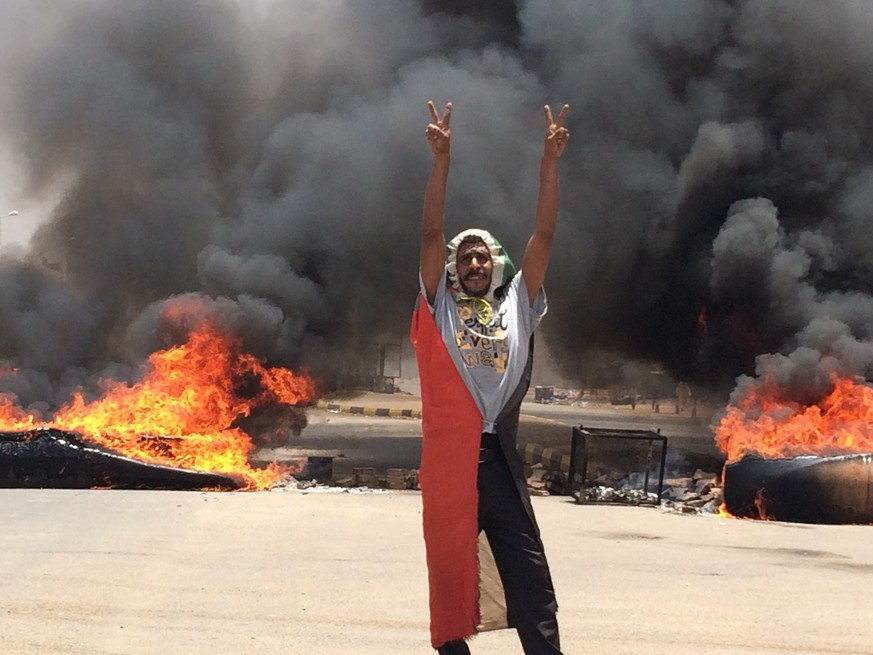 A protester flashes the victory sign in front of burning tires and debris on road 60, near Khartoum&#039;s army headquarters, in Khartoum, Sudan, Monday, June 3, 2019. Sudanese protest leaders say at  ...